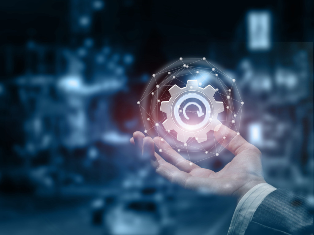 A male hand with an update cogwheel inside a digital sphere. A male hand with an update cogwheel inside a digital sphere.