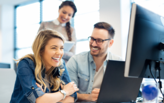 Three young professionals smile as they review a computer screen representing business process outsourcing.