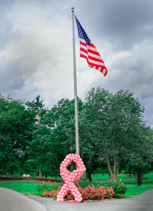 Flag Pole with American Flag and Cancer Awareness Ribbon in Balloons at the Base