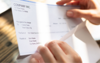 Close-up view of hands holding an open cheque from 'COMPANY INC.', with a focus on the cheque details against a sunlit background, representing the kind of financial document processing handled by an outsourced mailroom service.