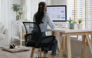 Woman at a desk scrolls her mouse on a screen with a dog nearby resting symbolizing work from home.