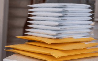 A stack of sealed padded envelopes, both white and yellow, sits on a countertop—ready for mailing. This image illustrates efficient mail handling, ideal for businesses using an office postage meter to streamline bulk shipping tasks and reduce mailing costs.