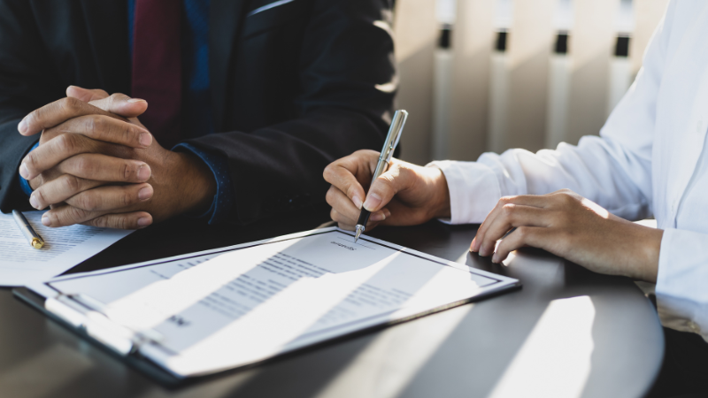 Close-up of two business professionals at a desk reviewing and signing a contract, representing a printer lease agreement in a corporate setting.