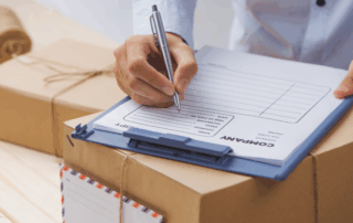 Close up of an employee filling out a mailing slip on top of a box with letters on a desk, signifying mailroom services.