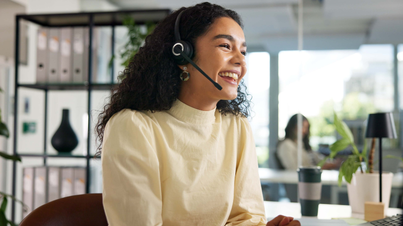 A smiling, happy customer service representative speaks on a headset in a modern office signifying copier service.