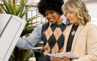 Two businesswomen stand over an MFP in an office
