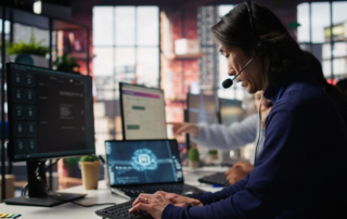 IT Support Services professional working at a computer workstation with multiple monitors, providing technical assistance in a modern office environment.